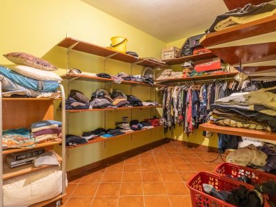Spacious walk-in closet featuring open wooden shelving, light yellow walls, and terracotta floor tiles, providing extensive storage capacity.