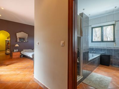 View from the hallway with terracotta tiles, showing a bedroom with dark walls and an ornate mirror on the left, and a tiled bathroom with a bathtub on the right.
