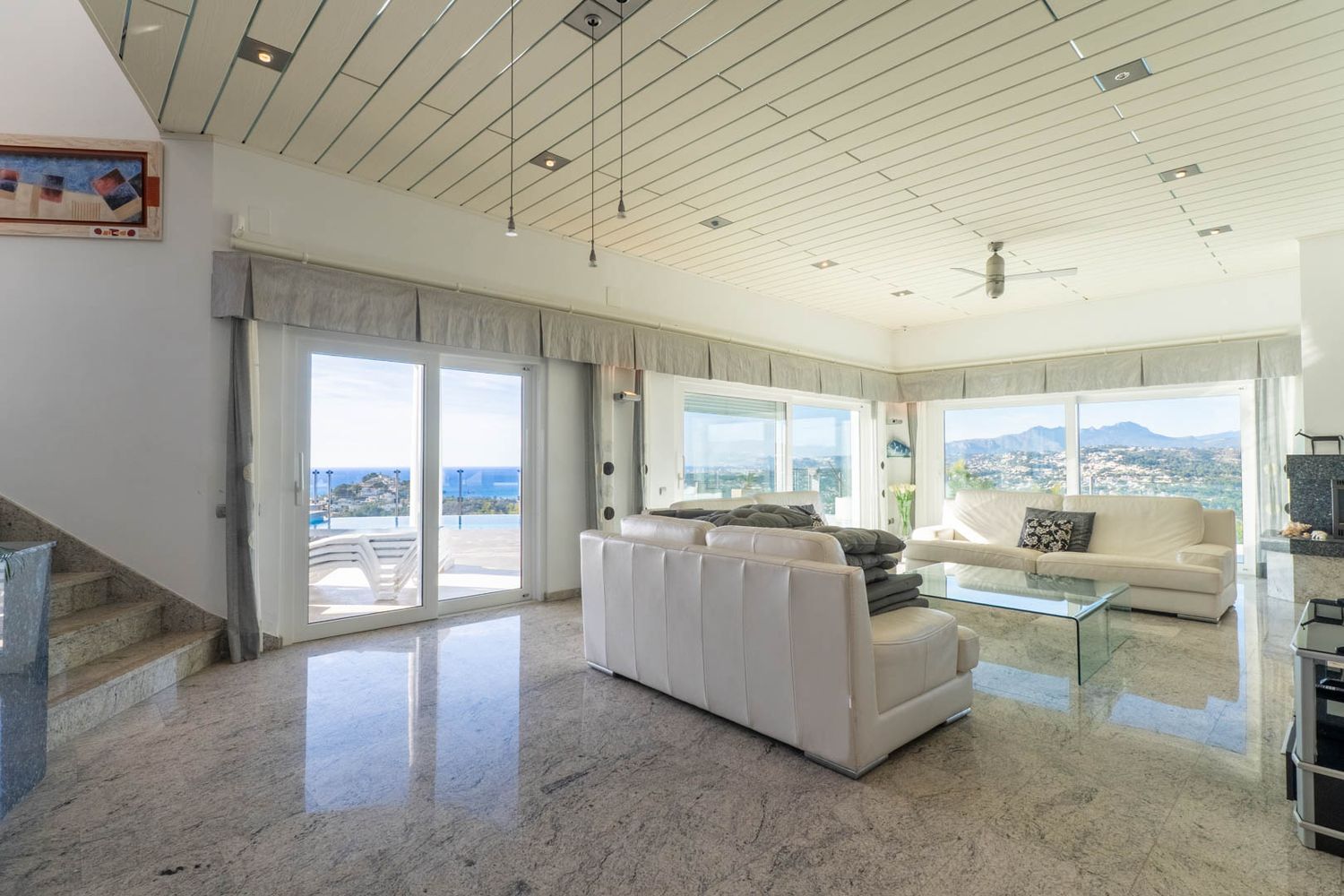 Spacious living room featuring polished granite floors, paneled ceilings, and panoramic sea and mountain views, with direct access to the terrace and pool.