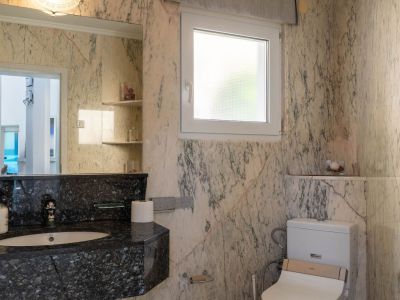 Bathroom featuring light veined marble walls, a dark granite vanity with an integrated sink, and a large mirror. It includes a frosted window and a toilet with bidet functionality.