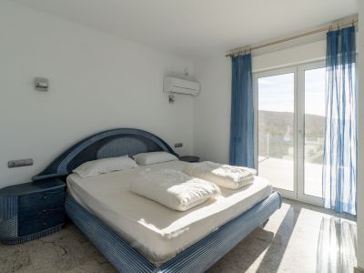 Bedroom featuring a blue patterned bed frame with matching nightstands, light-colored flooring, and direct access to a terrace through a glass door, offering hillside views and natural light.