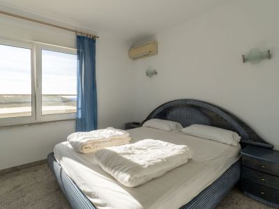 Bedroom featuring a blue patterned bed with a woven headboard, light tiled flooring, and an exterior view through the window. Equipped with air conditioning and a matching bedside table.