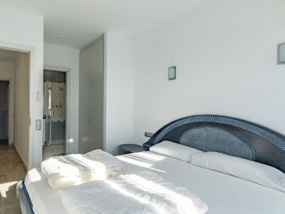 Bright bedroom featuring a double bed with a dark wood headboard and woven inlay. It includes a built-in wardrobe and direct access to an en-suite bathroom with a glass shower.
