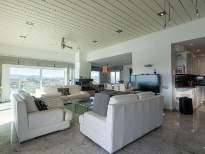 Bright living-dining area with white leather sofas, marble flooring, and large windows offering panoramic mountain views. The open-concept kitchen features dark granite countertops.