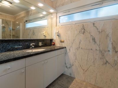 Elegant bathroom featuring veined marble walls and floor, a vanity with a dark granite countertop, and an integrated sink. A frosted horizontal window provides natural light and privacy.