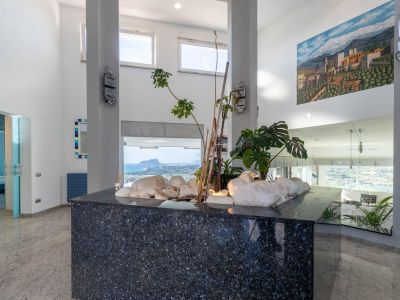 Entrance hall featuring a dark granite decorative island with white stones and plants. High ceilings and large windows frame panoramic sea views, including the iconic Peñón de Ifach.