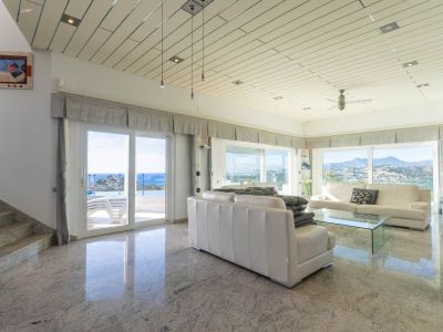 Spacious living room featuring polished granite floors, paneled ceilings, and panoramic sea and mountain views, with direct access to the terrace and pool.