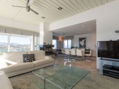 Spacious open-plan living and dining area featuring polished marble floors, a white sofa, and a dark stone fireplace. Large windows frame panoramic mountain and valley views.