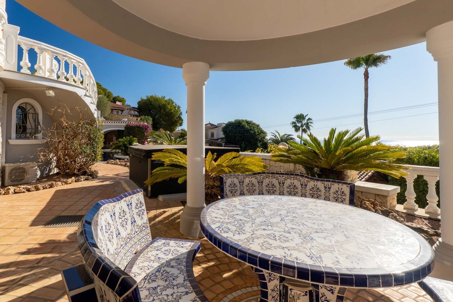 Covered outdoor terrace featuring a blue and white ceramic tiled table and benches, terracotta flooring, and partial Mediterranean sea views.