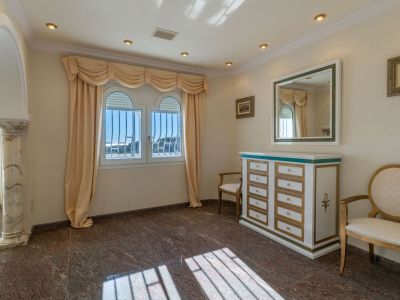 Auxiliary room featuring dark marble flooring, two arched windows with security bars, and beige drapes. A decorative chest of drawers with a mirror and a marble columned archway enhance the space.