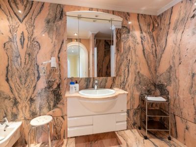 Bathroom clad in striking pink veined marble, featuring a white floating vanity beneath an illuminated mirrored cabinet and a bidet.