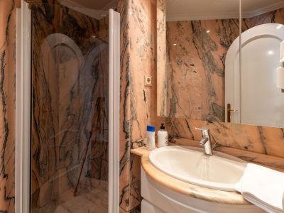 Bathroom featuring striking pink and black veined marble walls, a white ceramic sink, and a glass shower enclosure with a chrome faucet.