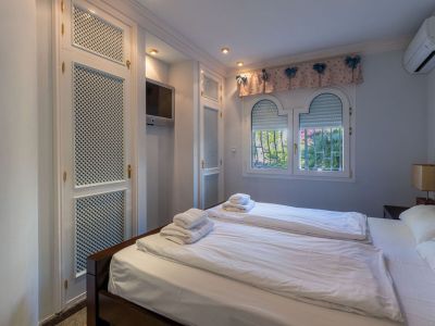 Bedroom featuring white louvered built-in wardrobes, a wall-mounted TV, and arched windows with garden views.