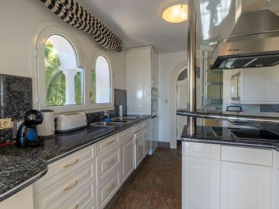 Bright kitchen featuring dark granite countertops, white cabinetry, and arched windows overlooking lush greenery. Equipped with a breakfast bar and modern appliances.