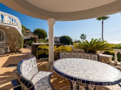 Covered outdoor terrace featuring a blue and white ceramic tiled table and benches, terracotta flooring, and partial Mediterranean sea views.
