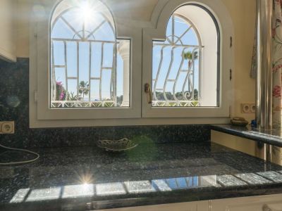 Dark granite countertop beneath two arched windows with decorative grilles, revealing partial sea and palm tree views. Direct sunlight illuminates the surface.