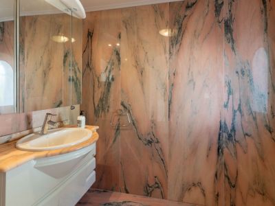 Elegant bathroom featuring walls and countertop clad in distinctive pink marble with dark veining. A white vanity with an oval sink and mirrored cabinet provides functionality.