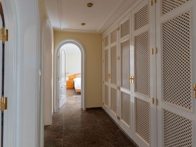 Elegant hallway featuring extensive white louvered built-in wardrobes with brass handles, dark tiled flooring, and arched doorways leading to bright rooms, including a bedroom.