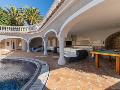 Expansive covered terrace featuring a curved pool, outdoor kitchen with barbecue, lounge seating, and a billiard table on terracotta flooring.