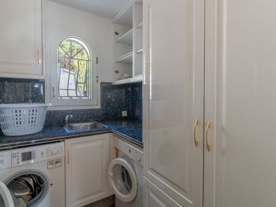 Functional utility room featuring dark granite countertops, a stainless steel sink, and washing machines. An arched window with a grate provides natural light, complemented by white cabinetry.