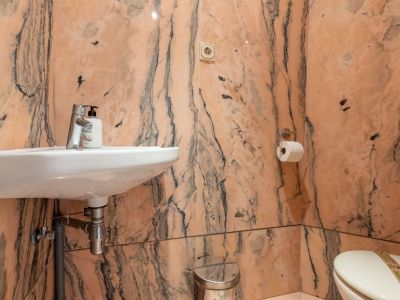 Guest toilet featuring walls and floor clad in pink veined marble. Equipped with a wall-mounted white sink, chrome faucet, and toilet.