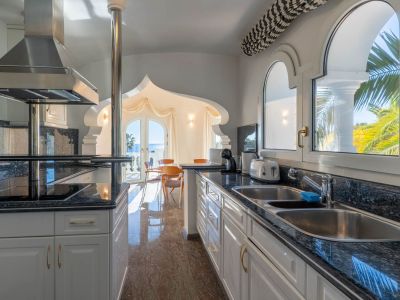 Independent kitchen featuring dark granite countertops and a double sink. Decorative arches frame the Mediterranean sea view and dining area, with polished marble flooring.