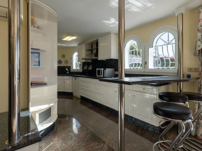 Independent kitchen featuring white cabinetry, dark granite countertops, and a breakfast bar with stools. Arched windows offer views of the exterior, complemented by a polished reddish-brown floor.