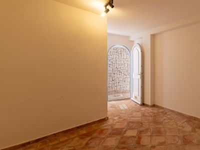 Interior hallway featuring terracotta tiled flooring and an arched white door opening to an outdoor patio with an irregular stone wall. Ceiling spotlights.