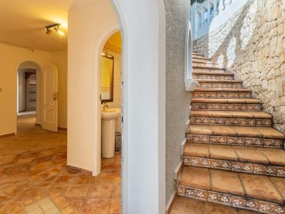 Interior hallway with terracotta tiled floors and arched entrances, contrasting with an exterior stone staircase featuring decorative risers and a robust stone wall.