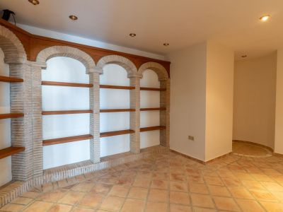 Interior room featuring terracotta floor tiles and a built-in shelving unit with brick arches and wooden shelves. Recessed lighting illuminates a distinct corner.