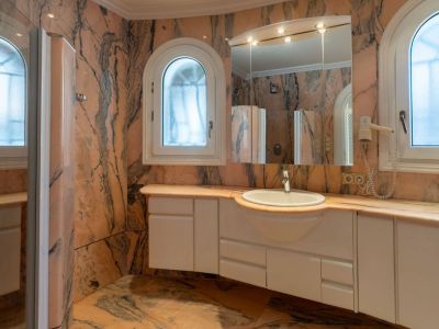 Main bathroom clad in veined pink marble, featuring a white floating vanity with integrated sink and two arched frosted windows.