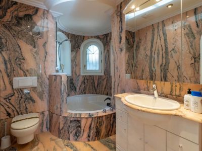 Main bathroom featuring pink and black veined marble, a built-in bathtub in a curved alcove, and an arched window providing natural light.