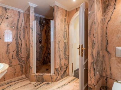 Main bathroom fully clad in veined pink marble, featuring a walk-in shower with a glass screen and an arched doorway.