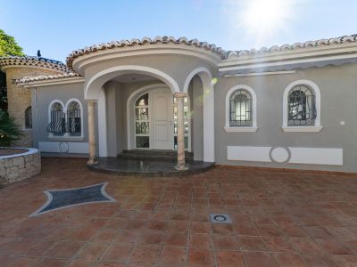 Main entrance of the villa featuring a curved porch with marble columns and white arches. Arched windows with decorative wrought iron grilles and terracotta paving.