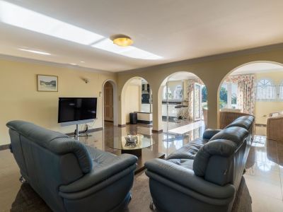 Spacious living area featuring glossy dark marble floors, leather sofas, and arched openings leading to the kitchen and outdoor terrace. Natural light fills the room.