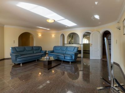 Spacious living area featuring polished dark marble floors, blue leather sofas, and multiple arched openings leading to adjacent rooms. Natural light reflects on the ceiling.
