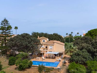 Aerial view of the two-story villa with tiled roof, showcasing the blue swimming pool, paved terrace with pergola, and expansive Mediterranean garden.