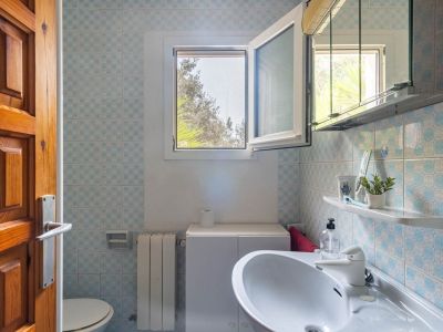 Bathroom featuring blue and white patterned tiles, a white sink with under-cabinet storage, and an open window providing natural light and green outdoor views.