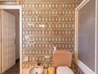Bathroom with green and beige patterned tiles, pink toilet and bidet, frosted shower screen, and a speckled terrazzo floor.