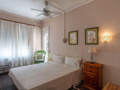 Bedroom featuring a double bed, wooden nightstand with lamp, and a ceiling fan. Includes a green wicker chair and glass door access to the exterior.