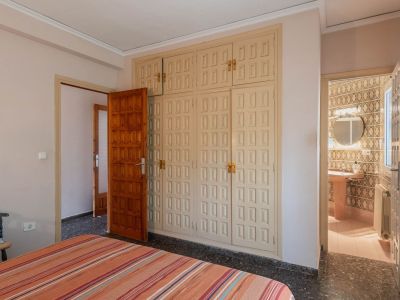 Bedroom featuring a large, light-colored built-in wardrobe with panelled doors and dark terrazzo flooring, offering direct access to a tiled bathroom.