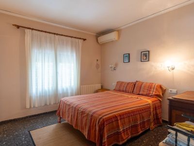 Double bedroom featuring striped bedding, a window with sheer curtains, dark flooring, and an air conditioning unit.