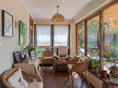 Enclosed terrace featuring large wooden-framed windows, tiled floor, wicker seating, and a stained-glass pendant lamp, overlooking the garden.
