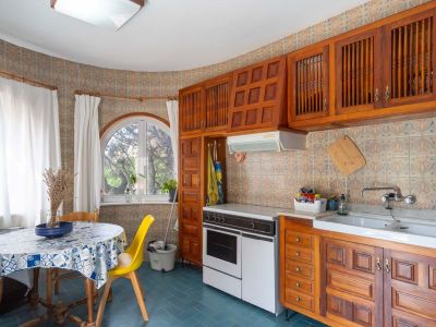 Functional kitchen featuring traditional wooden cabinetry, patterned wall tiles, and an arched window. Includes a dining area with a round table and natural light.