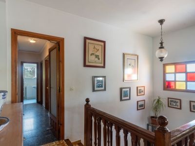 Hallway featuring a traditional wooden staircase and banister. A distinctive window with colored glass panes and framed art adorn the white wall.