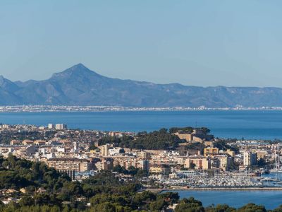Panoramic view of Dénia, showcasing its historic castle, bustling marina, and urban landscape against the Mediterranean Sea and Montgó mountain range.