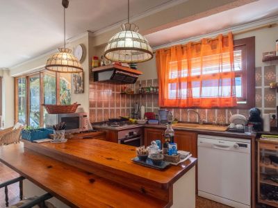 Rustic style kitchen featuring a wooden breakfast bar, patterned tiles, integrated appliances, and a view into an enclosed terrace.