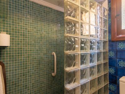 Shower area featuring teal mosaic tiles, a glass block partition, and a white grab bar. A wooden-framed window with textured glass is visible nearby.