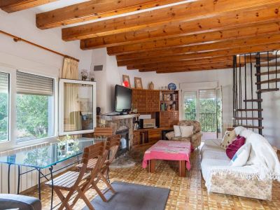 Spacious living area featuring exposed wooden beams, a stone fireplace, and patterned floor tiles. Includes a glass dining table and a spiral staircase.