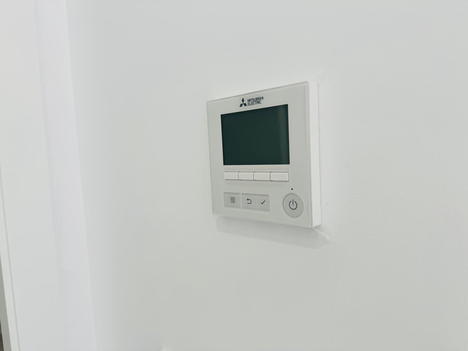 Mitsubishi Electric control panel for ducted air conditioning, featuring a digital display and intuitive buttons, integrated seamlessly into the white wall.
